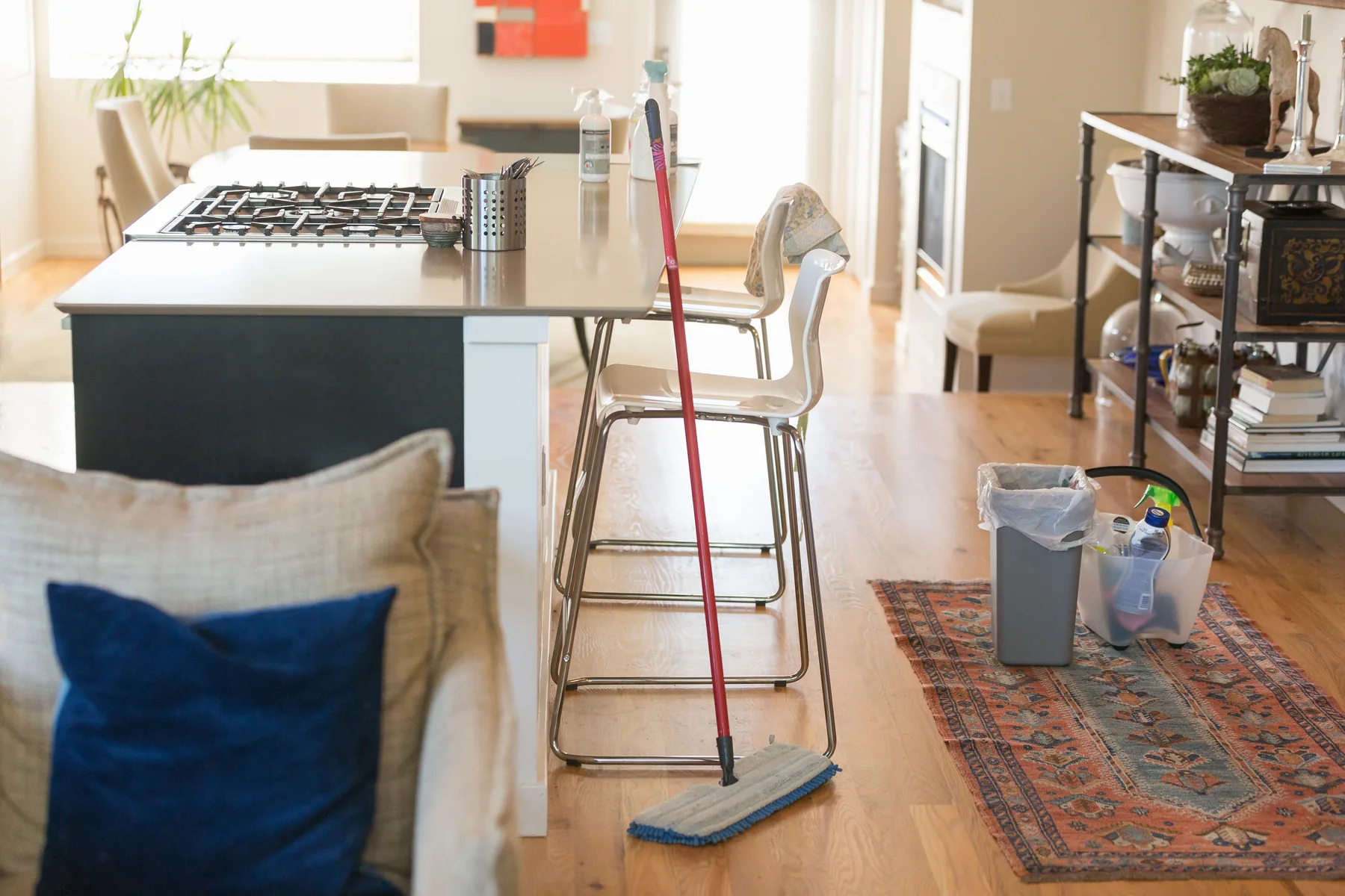 A mop and a caddy of cleaning products ready for work in a bright open-plan kitchen and living room