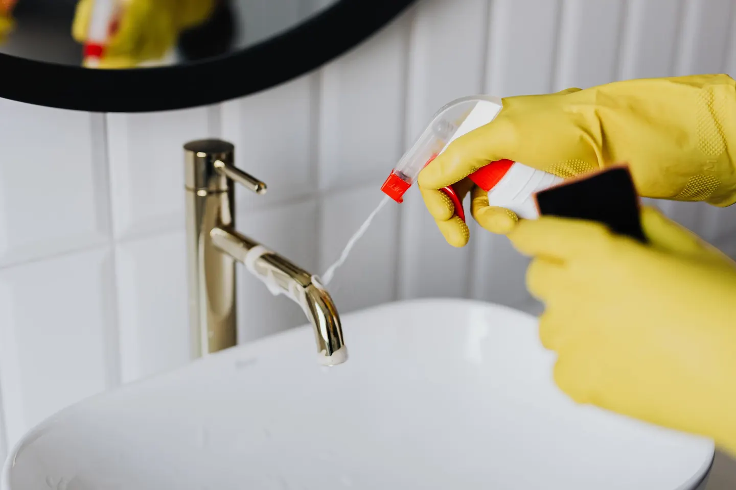 Gloved hands spraying and wiping a brass basin tap