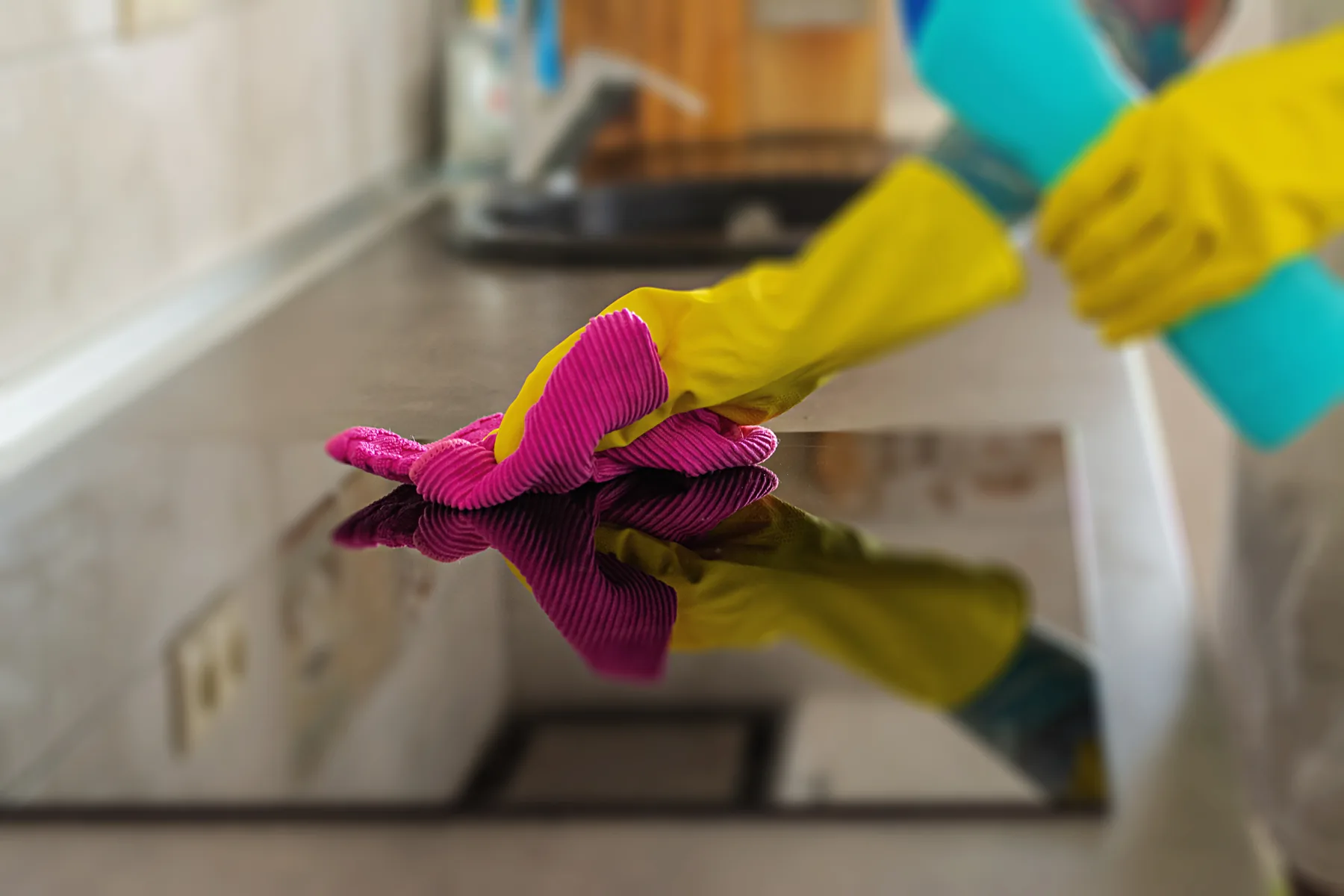 Gloved hands polishing a glass hob and kitchen worktop before a tenancy handover