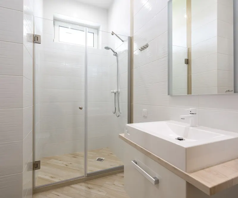 A clean white-tiled bathroom with a glass shower enclosure, basin and mirror cabinet